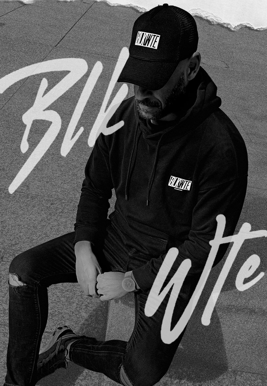 Person wearing a black hoodie and cap with 'BLK WTE' branding, sitting on a textured surface.