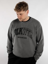 Male wearing a grey stonewash sweatshirt with 'BLKWTE' college style logo printed across the front in black