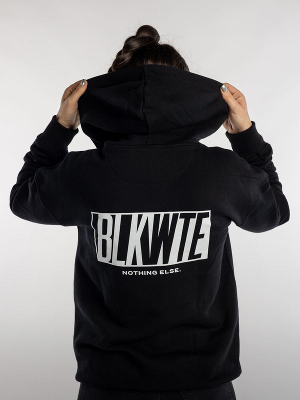 Female wearing a black hoodie with 'BLKWTE' branding on the back against a white background
