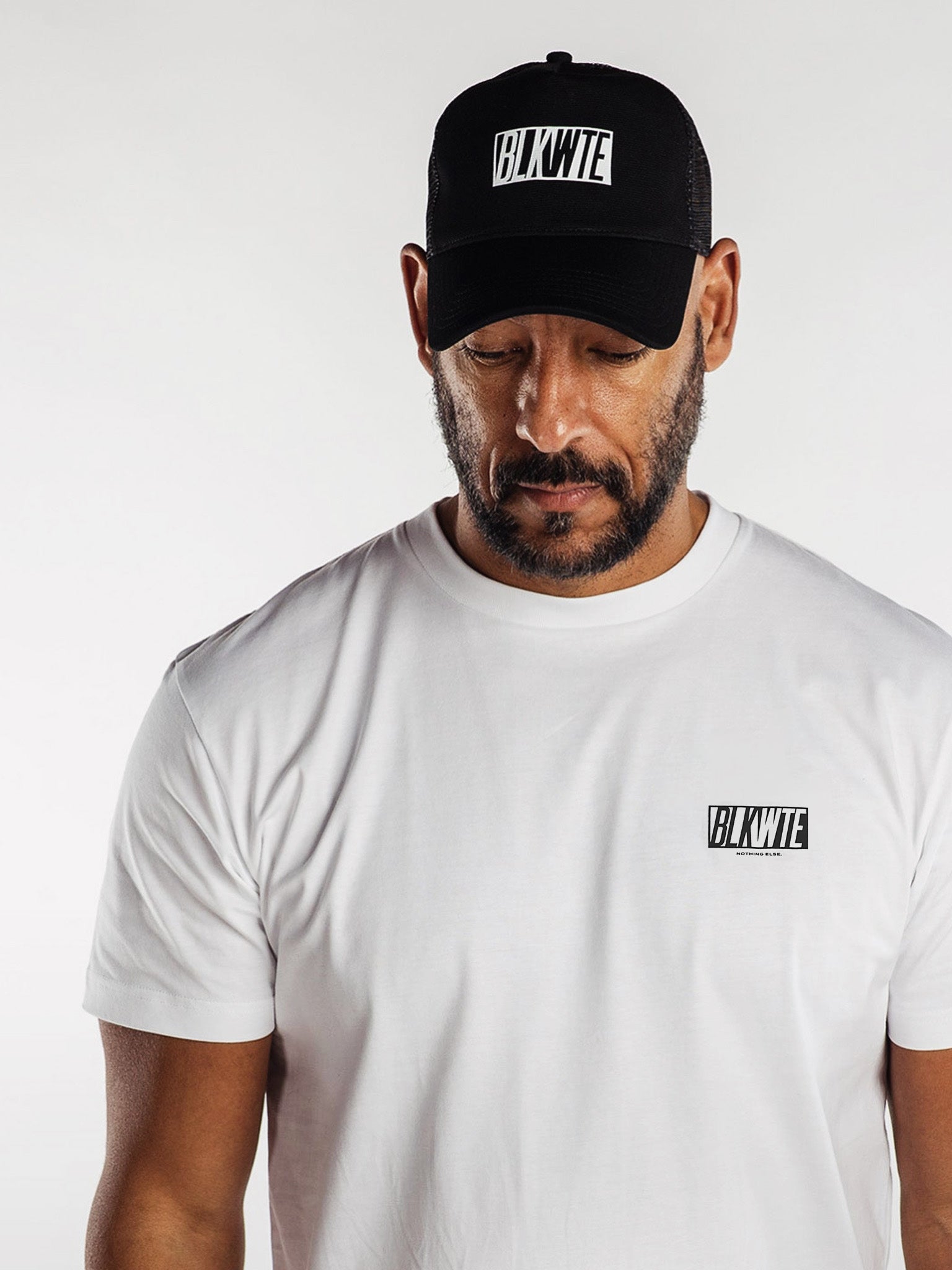 Man wearing a black cap and white t-shirt with 'BLKWTE' branding on a white background