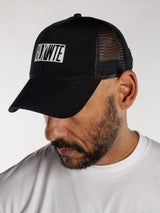 Male wearing a all black trucker cap with BLKWTE logo across the front