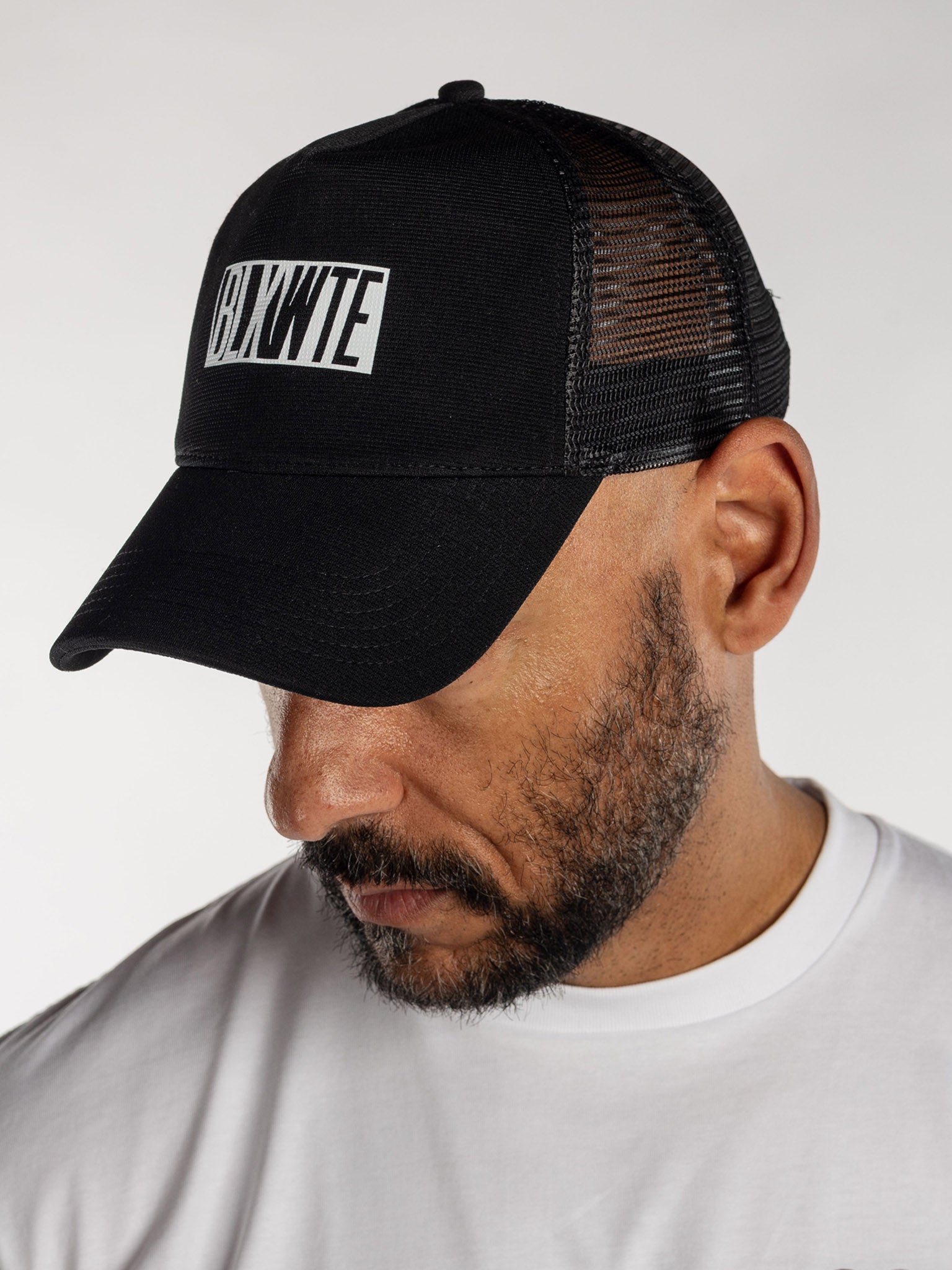 Male wearing a all black trucker cap with BLKWTE logo across the front