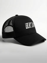 Black trucker cap with 'BLKWTE' logo on the front panel on a light gray background