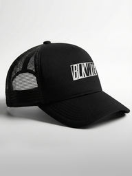 Black trucker cap with 'BLKWTE' logo on the front panel on a light gray background
