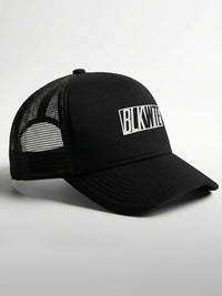 Black trucker cap with 'BLKWTE' logo on the front panel on a light gray background